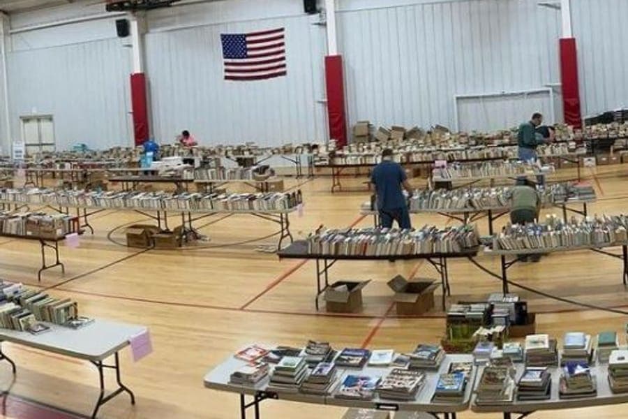 Rows of tables covered with donated books in a gymnasium, with a few people browsing