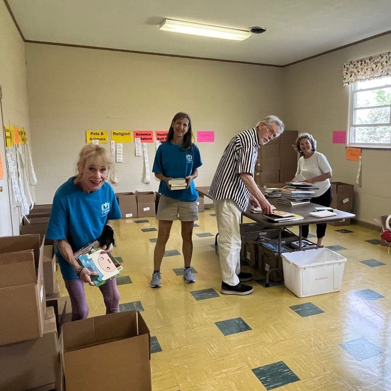 Volunteers sorting donated books at tables in a room lined with boxes and subject signs