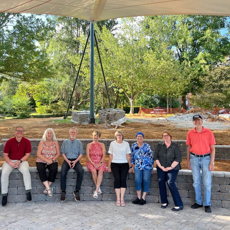 A group seated on the stone wall of the terrace under the shade sail, with trees behind them