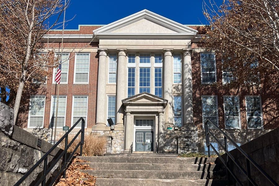 Concrete steps leading up to the columned entrance of the brick Staunton Public Library under a clear blue sky, with fallen leaves along one side